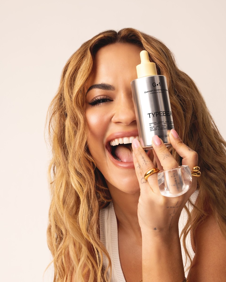 Rita Ora laughing, holding G&middot;1 to her face